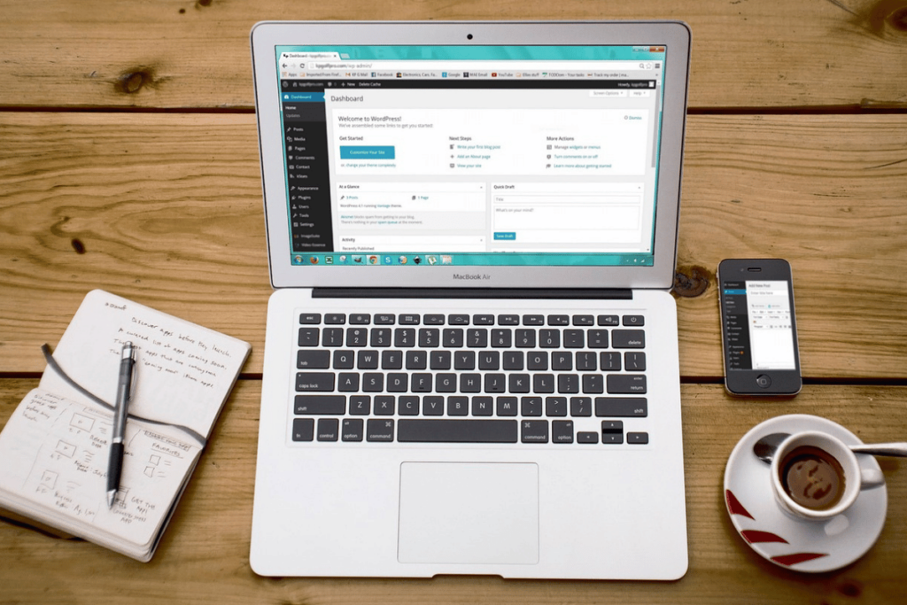Top-down view of a MacBook Air on a wooden desk, with WordPress open and a notebook alongside.