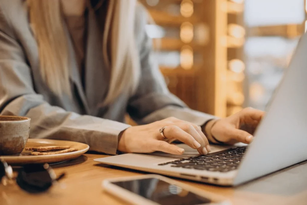 Professional working on a laptop at a café with a hot beverage and smartphone on the table.