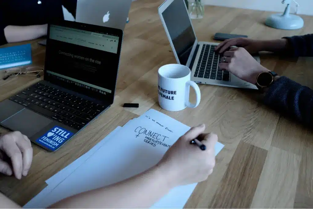 Team members engaged in a planning session at a modern workspace with laptops open to a women's network site.