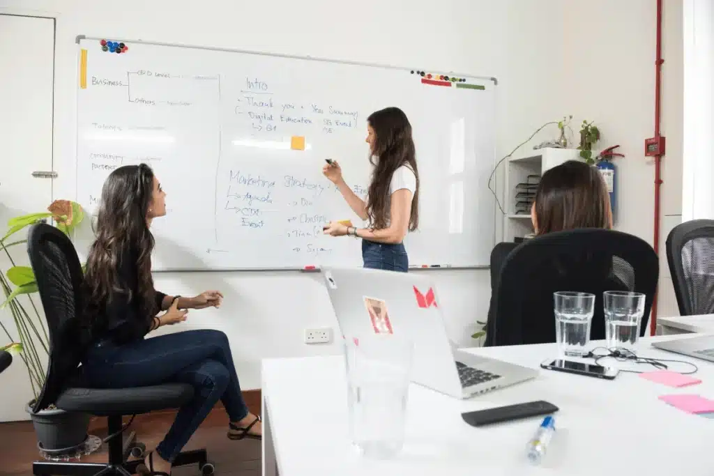 Women brainstorming ideas and writing on a whiteboard during a meeting.