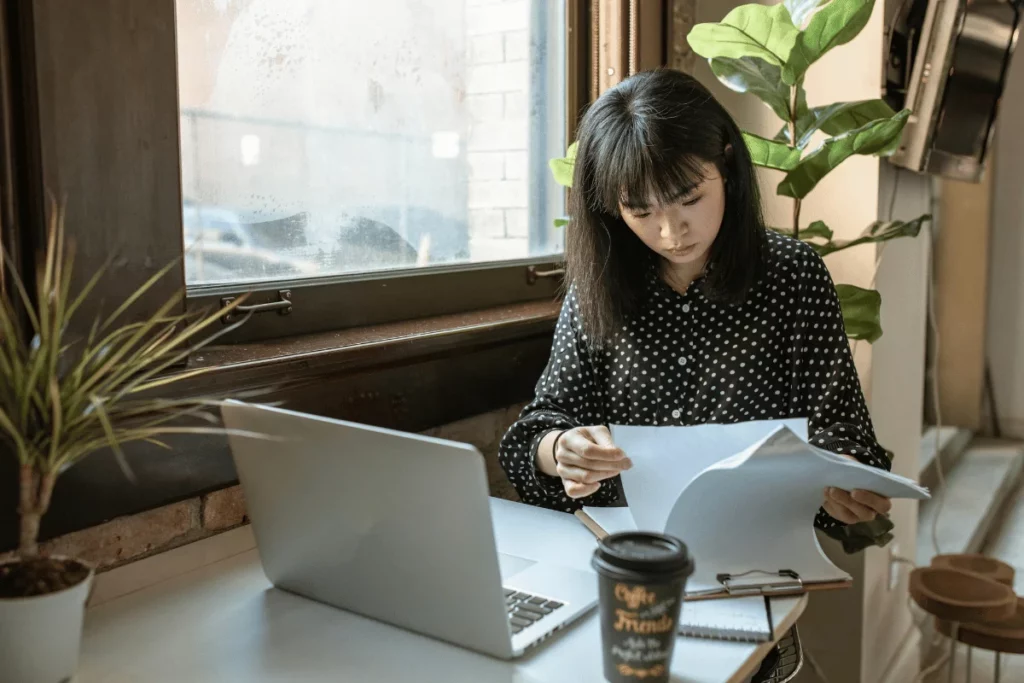 Woman reviewing documents while working on a laptop.