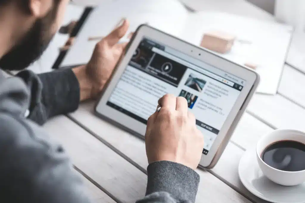 Close-up of hands using stylus on a tablet next to a cup of coffee.
