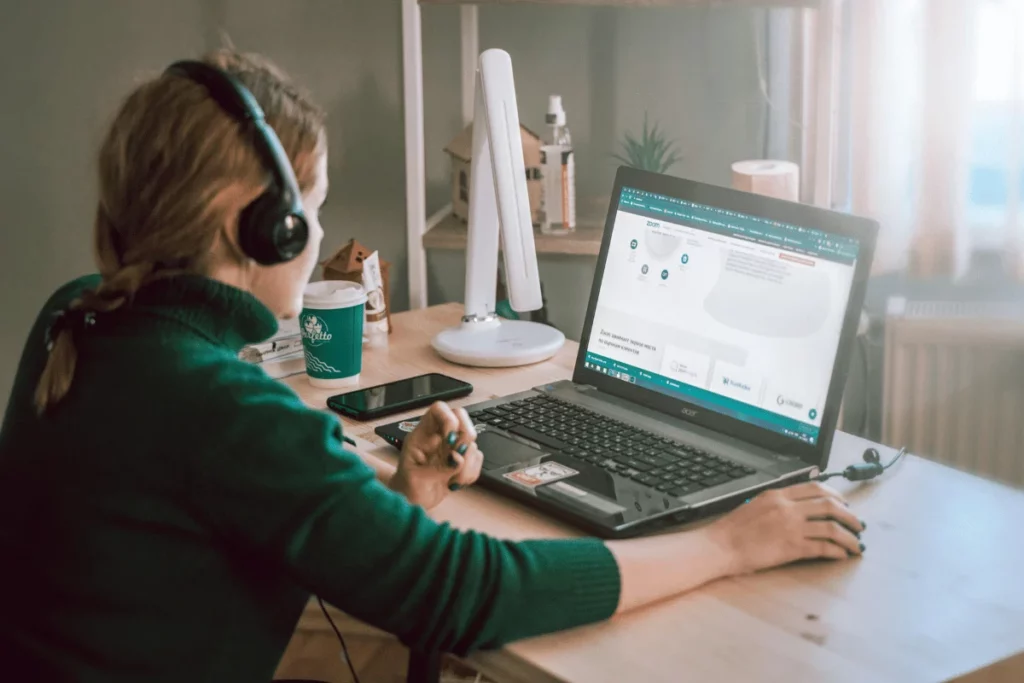 Woman wearing headphones while working on a laptop at a home office desk.