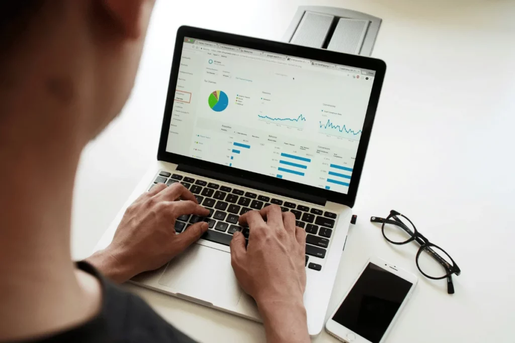 Hands typing on a laptop showing website analytics and performance graphs.