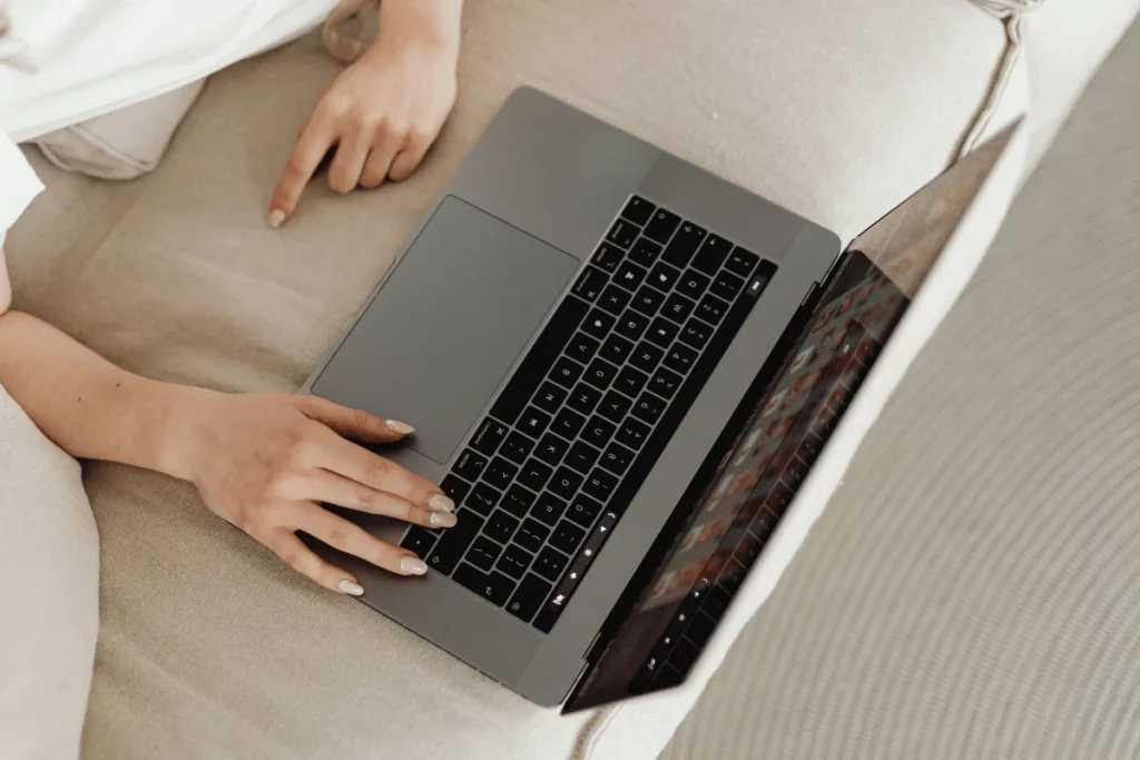 Person casually using a laptop on a beige sofa at home.