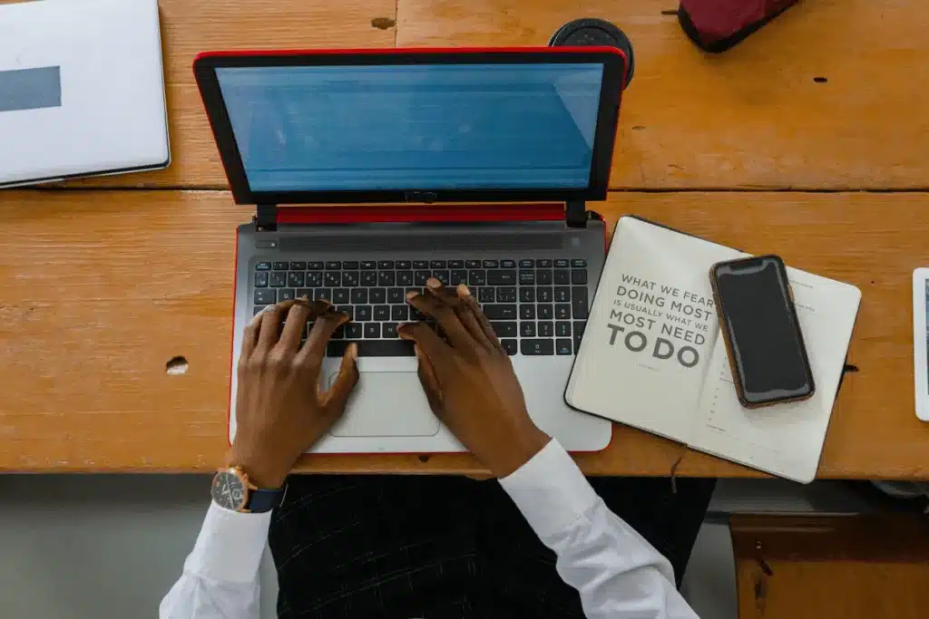 Hands typing on a laptop with a red frame on a wooden desk.