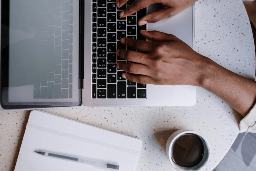Overhead shot of hands typing on a MacBook beside a coffee cup.