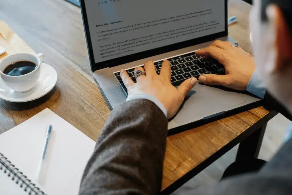 Businessman composing a letter on laptop with coffee and notepad on desk.