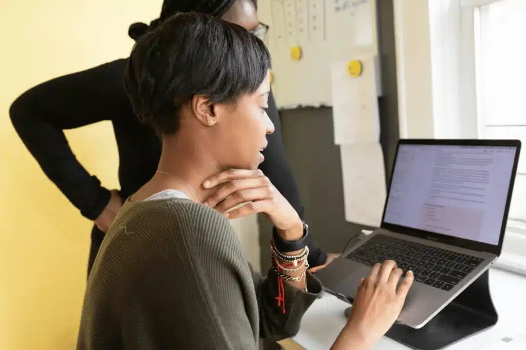 Female professional typing on a laptop, while another person observes.