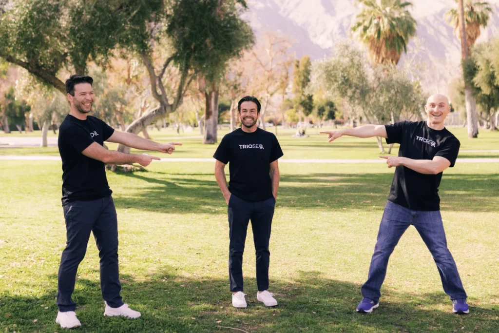 Smiling trio Steven, Connor, and Nathan model black TRIOS® t-shirts outside.