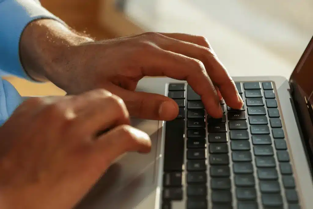 Person working on a laptop, sunlight highlighting active typing hands.