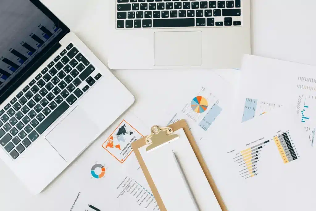 Top-down view of a business analyst’s desk with laptops open on statistical data and printed charts.