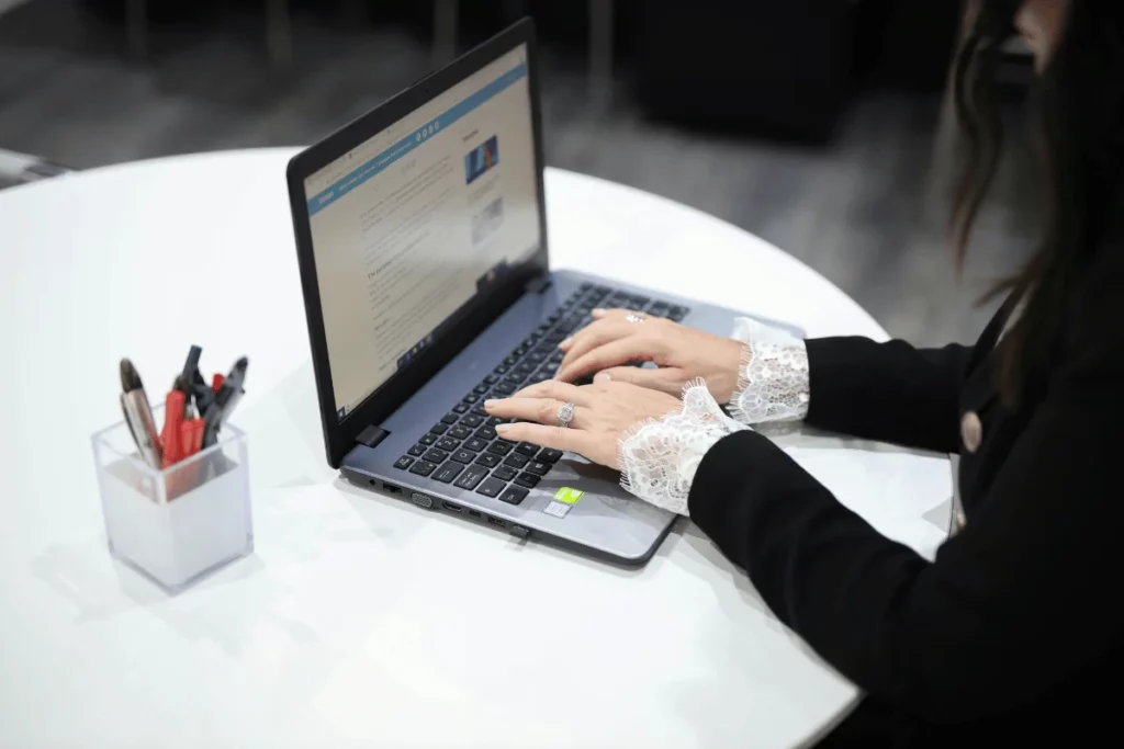 Woman typing on a laptop at a white table, focused on an online article.