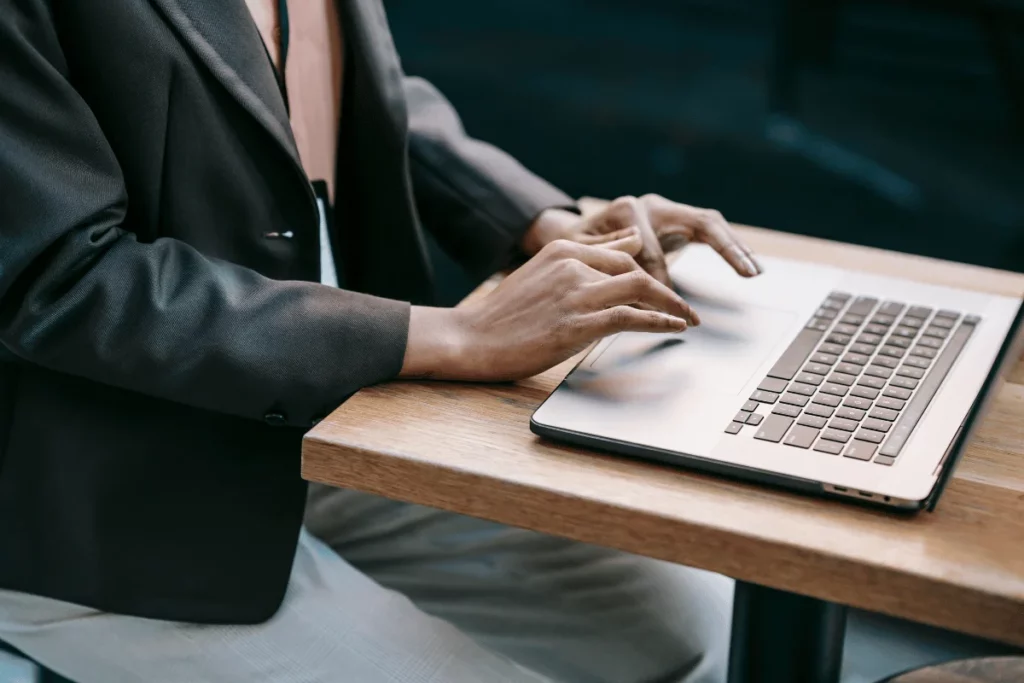 Close-up of hands typing on a laptop, person wearing a business jacket.